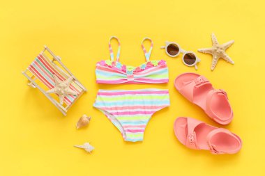 Sarı arka planda plaj aksesuarları olan çocuk mayosu.