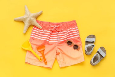 Sarı arka planda plaj aksesuarları olan çocuk yüzme şortu.