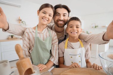 Happy father with his children taking selfie while cooking in kitchen
