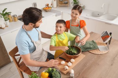 Happy father with his children making vegetable salad in kitchen