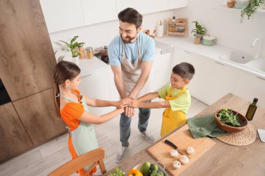 Happy father with his children putting hands together before cooking in kitchen