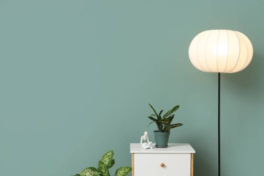 Yeşil duvarın yanındaki masada parlayan lamba ve bitki