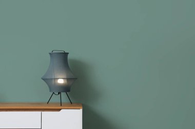 Yeşil duvarın yanındaki çekmecelerin üzerinde şık bir lamba