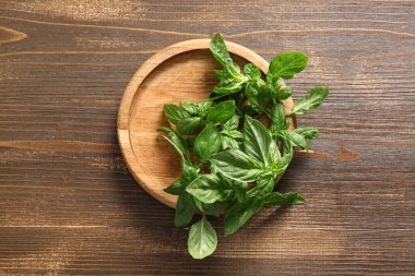 Ahşap arka planda taze yeşil fesleğen yapraklı tabak.