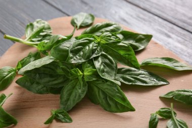 Gri ahşap arka planda taze fesleğen yaprağı kesme tahtası, yakın plan.