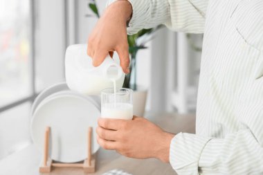 Young man pouring milk into glass in kitchen, closeup