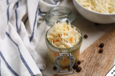 Lezzetli lahana turşulu kavanoz ve beyaz arka planda biber, yakın plan.