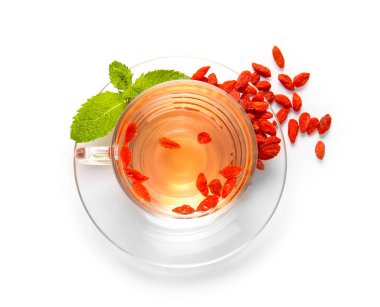 Bir bardak sıcak goji çayı ve beyaz arka planda nane ve böğürtlen.