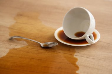 Kaşıkla ters çevrilmiş fincan ve mutfaktaki masaya dökülmüş kahve, yakın plan.