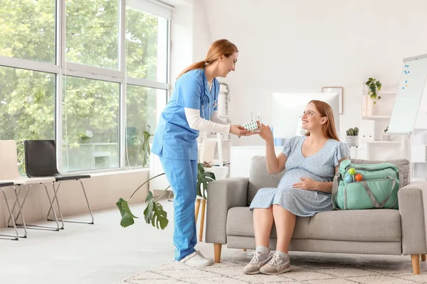 Young pregnant woman taking pills from doctor on sofa in clinic