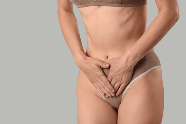 Young woman in panties suffering from menstrual cramps on grey background, closeup