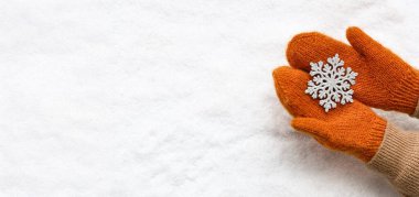 Hands in warm mittens and with decorative snowflake on snowy background with space for text