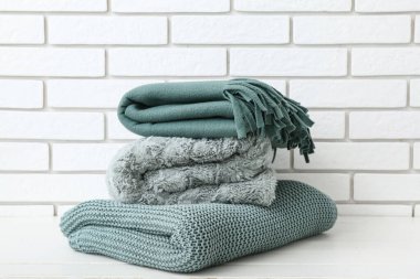 Hafif tuğla duvarın yanındaki masada yeni katlanmış battaniyeler.