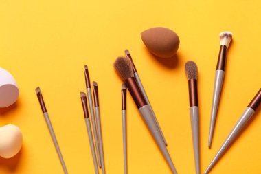Turuncu arka planda makyaj süngerleri ve fırçalar