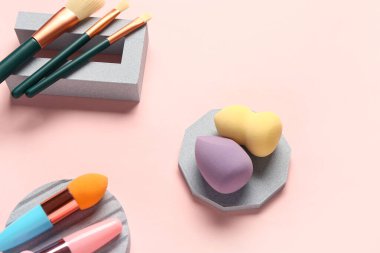 Pembe arka planda makyaj süngerleri ve fırçaları olan dekoratif podyumlar