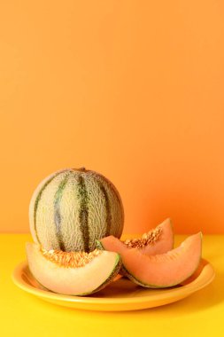 Lezzetli olgun kavunlu tabak ve turuncu arka planda dilimler.