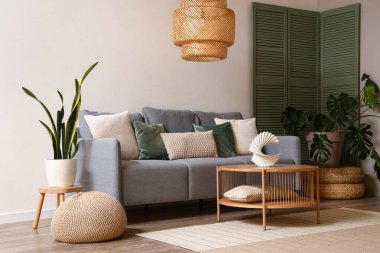 Modern oturma odasının içinde gri kanepe, yeşil katlanmış ekran ve kahve masası.