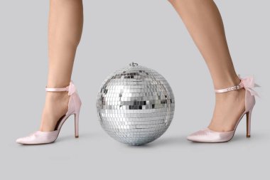 Gri arka planda disko topu olan şık topuklu kadın bacakları.