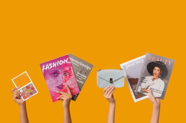Female hands with different magazines, stylish bag and palette of eyeshadows on yellow background