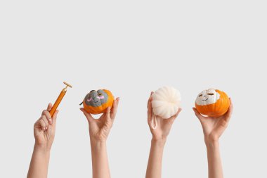 Female hands holding pumpkins with drawn faces, bath sponge and facial massage tool on white background