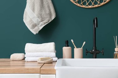 Lavabo ve banyo aksesuarları banyodaki yeşil duvarın yanında.