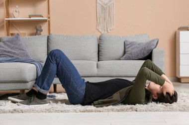Depresyondaki genç adam evde halıda yatıyor.