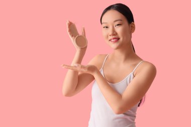 Beautiful Asian woman with makeup powder on pink background