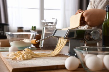 Mutfaktaki masada makineyle makarna yapan genç kadın, yakın plan.