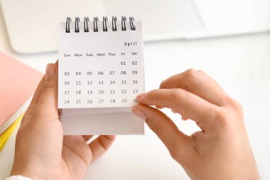 Female hands with flip calendar at table in office, closeup