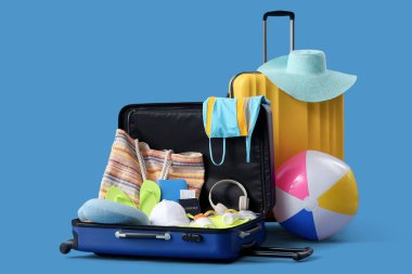 Mavi arka planda mayo, kulaklık ve plaj aksesuarları olan bavullar.