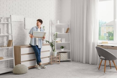 Evindeki beyaz tuğlalı duvarda resimleri olan genç bir adam.