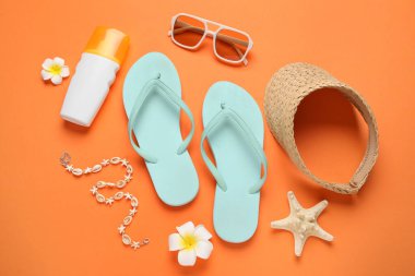 Şık plaj ayakkabılarıyla kompozisyon, bir şişe güneş kremi ve turuncu arka planda aksesuarlar, yakın plan.