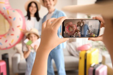 Little girl with mobile phone taking picture of her family at home, closeup. Travel concept