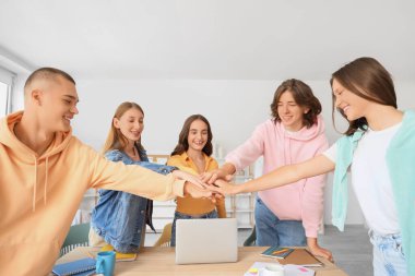 Group of students putting hands together at table in classroom