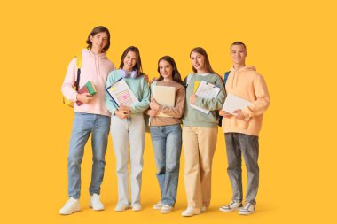 Group of students with laptops and books on yellow background