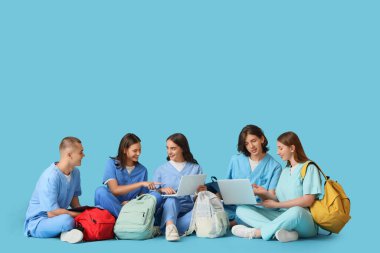 Group of medical students with laptops and backpacks sitting on blue background