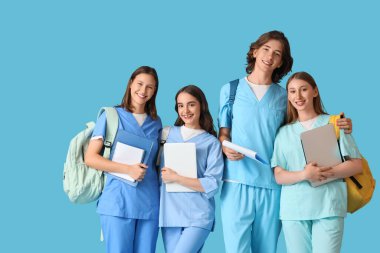 Mavi arka planda sırt çantalı ve dizüstü bilgisayarlı bir grup tıp öğrencisi.