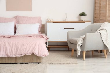 Bed with stylish pink bedding, folding screen, commode and armchair in bedroom