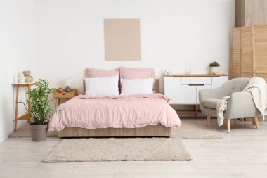 Bed with stylish pink bedding, folding screen, commode, armchair, table and houseplants in bedroom