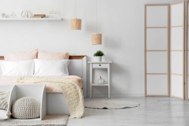 Bed with stylish pink bedding, folding screen, bedside table and home decor on shelf in bedroom