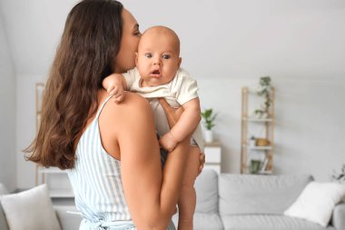 Beautiful young happy mother kissing her cute little baby at home