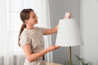 Beautiful young happy woman changing light bulb in floor lamp at home