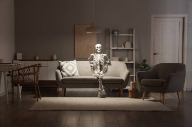 Geceleri oturma odasındaki gri koltukta oturan insan iskelet modeli.