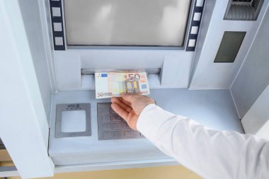 Male hand withdrawing euro banknotes from ATM outdoors, closeup