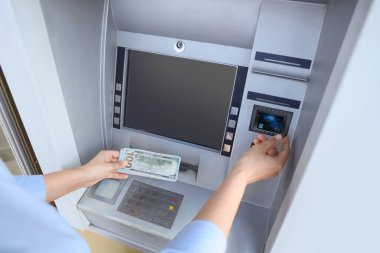 Businesswoman with credit card withdrawing dollar banknotes from ATM outdoors, closeup
