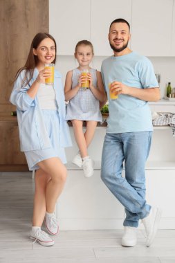 Happy parents with their little daughter and glasses of juice in kitchen