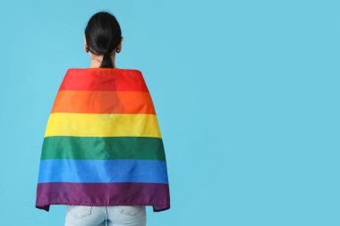 Young woman with ear tunnels and LGBT flag on blue background, back view