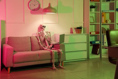 Human skeleton model with laptop on sofa in dark office