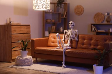 Geceleri oturma odasında deri koltukta oturan insan iskelet modeli.