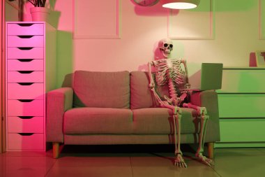 Human skeleton model with laptop on sofa in dark office